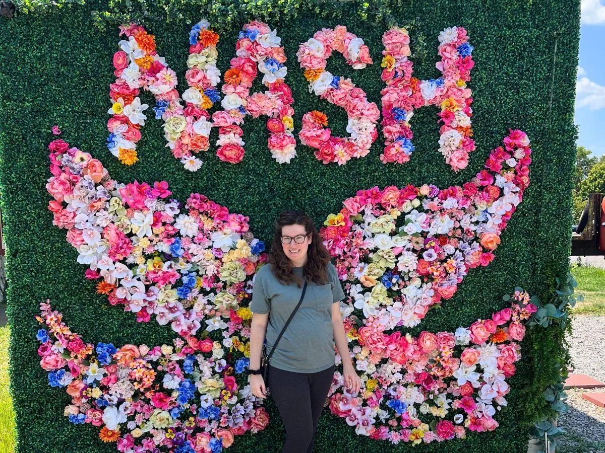 Visitor posing in front of the flower wings mural at 12 South spelling out NASH